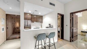 Una cucina moderna con un piano di lavoro bianco, due sgabelli da bar e una cappa aspirante in acciaio inox.