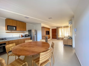 A modern kitchen with built-in appliances, a dining area with wicker chairs, and a view of the living room. - Residencial Saint Loius (Porto Seguro)
