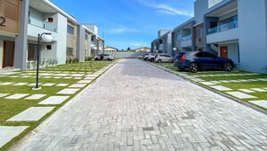 Ein modernes Wohngebäude mit gepflastertem Weg, parkenden Autos und blauem Himmel.