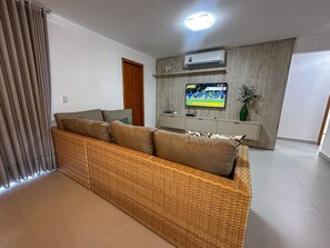 A living room with a sofa, a television, and an air conditioning unit. - Residencial Saint Loius (Porto Seguro)
