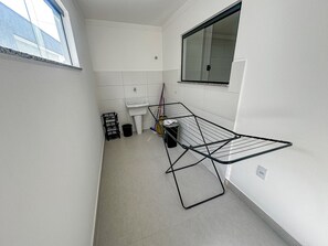 A narrow hallway with a window, a sink, a mop, and a metal drying rack. - Residencial Saint Loius (Porto Seguro)