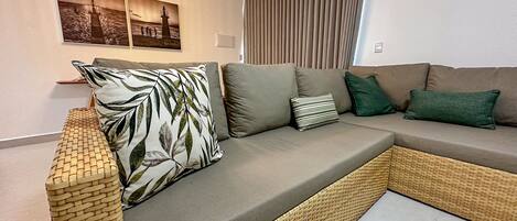 A modern living room with a sectional sofa, a woven bench, and a wall-mounted light fixture.