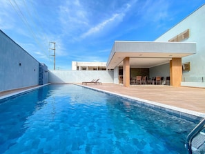 A swimming pool with a modern outdoor seating area and a building with a flat roof. - Residencial Saint Loius (Porto Seguro)
