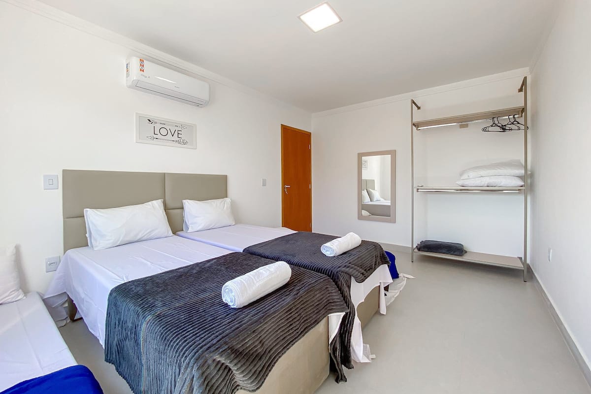 A hotel room with two beds, a wardrobe, a mirror, and a wall-mounted air conditioner.