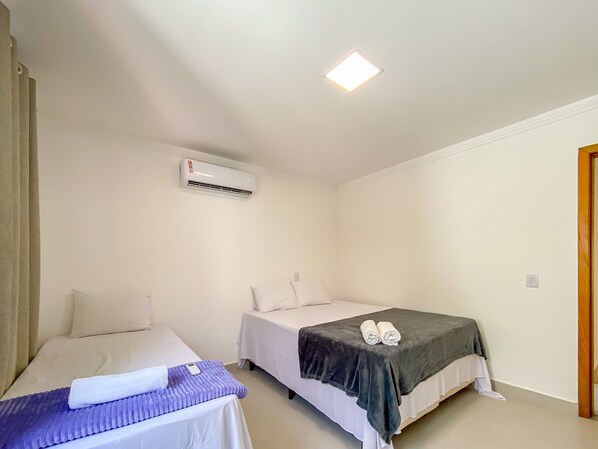 A hotel room with two beds, a ceiling light, an air conditioning unit, and a door. - Residencial Saint Loius (Porto Seguro)