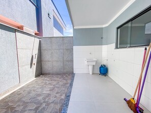 A narrow hallway with a tiled floor, a blue gas cylinder, a white sink, and a window. - Residencial Saint Loius (Porto Seguro)