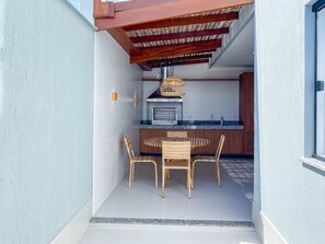 A modern outdoor kitchen with a built-in grill, a dining table with wicker chairs, and a pergola overhead. - Residencial Saint Loius (Porto Seguro)