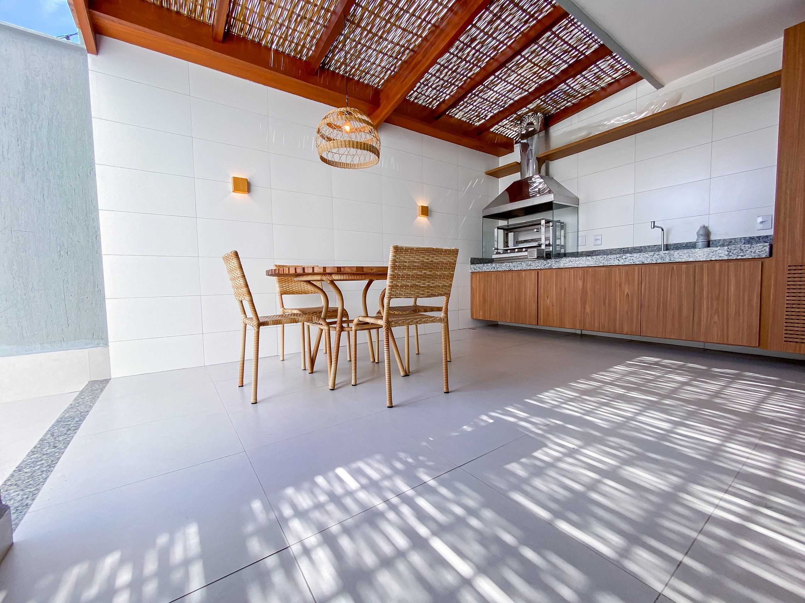 A modern kitchen with a dining area, featuring a wooden table and chairs, a hanging light fixture, and a kitchen island with a built-in oven.