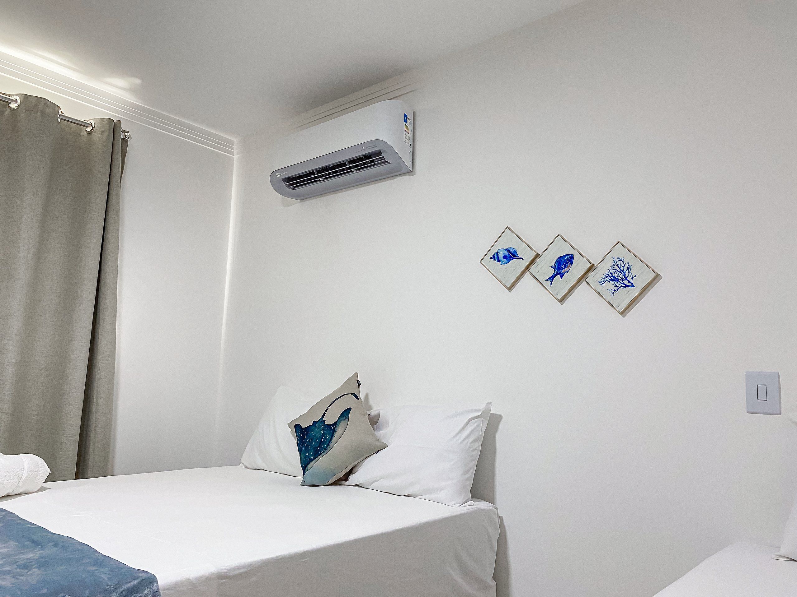 A hotel room with a bed, an air conditioning unit, and wall-mounted artwork.