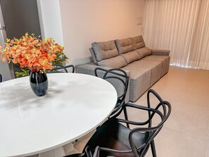 A dining area with a round table, chairs, a sofa, and a vase of flowers. - Residencial Saint Loius (Porto Seguro)