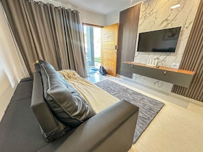A modern living room with a sofa, a flat-screen TV mounted on a marble wall, and a sliding door leading to an outdoor area. - Residencial Saint Loius (Porto Seguro)