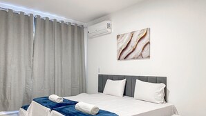 Ein Hotelzimmer mit Bett, Kopfteil, Wandklimaanlage und einem fensterbepflanzten Fenster.