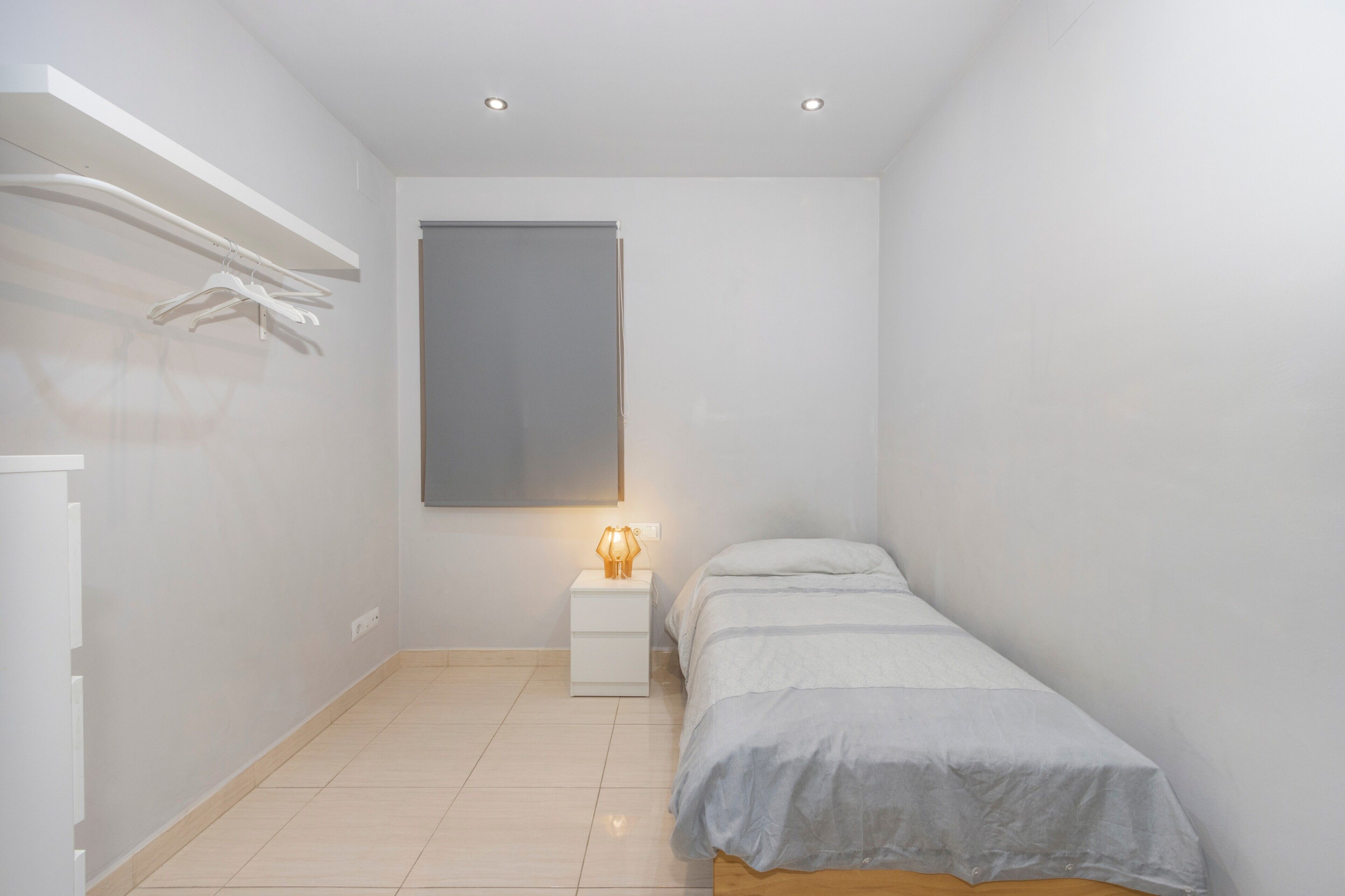 Une chambre à coucher avec un lit, une table de chevet et une étagère fixée au mur.