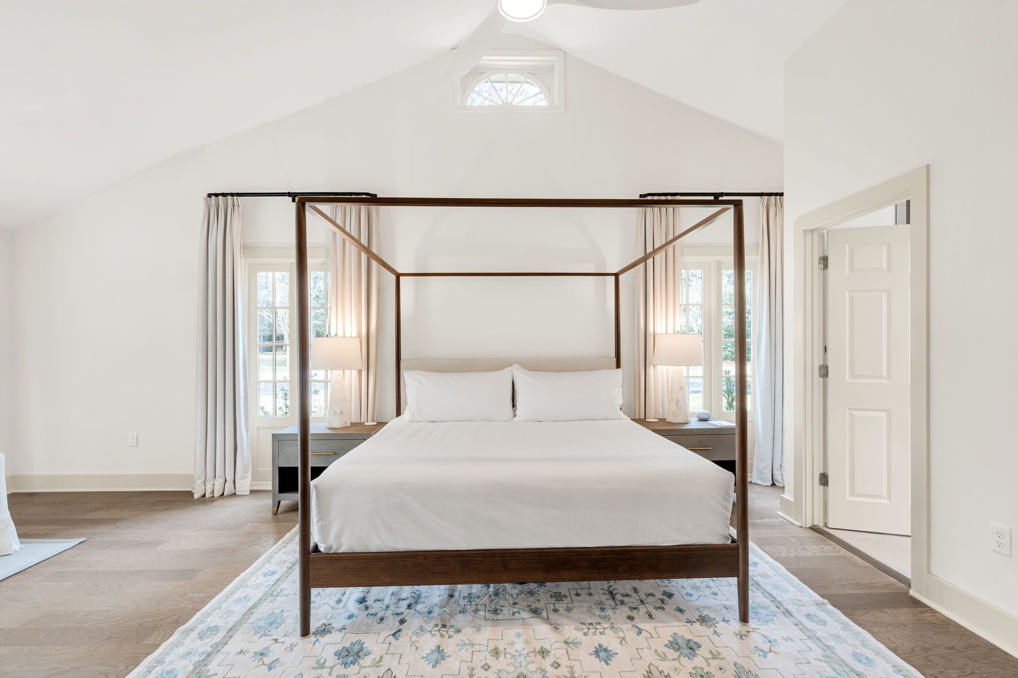Un lit à baldaquin avec une structure en bois, une literie blanche et un tapis à motifs floraux.