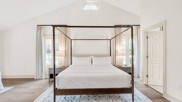 Un lit à baldaquin avec une structure en bois, une literie blanche et un tapis à motifs floraux.