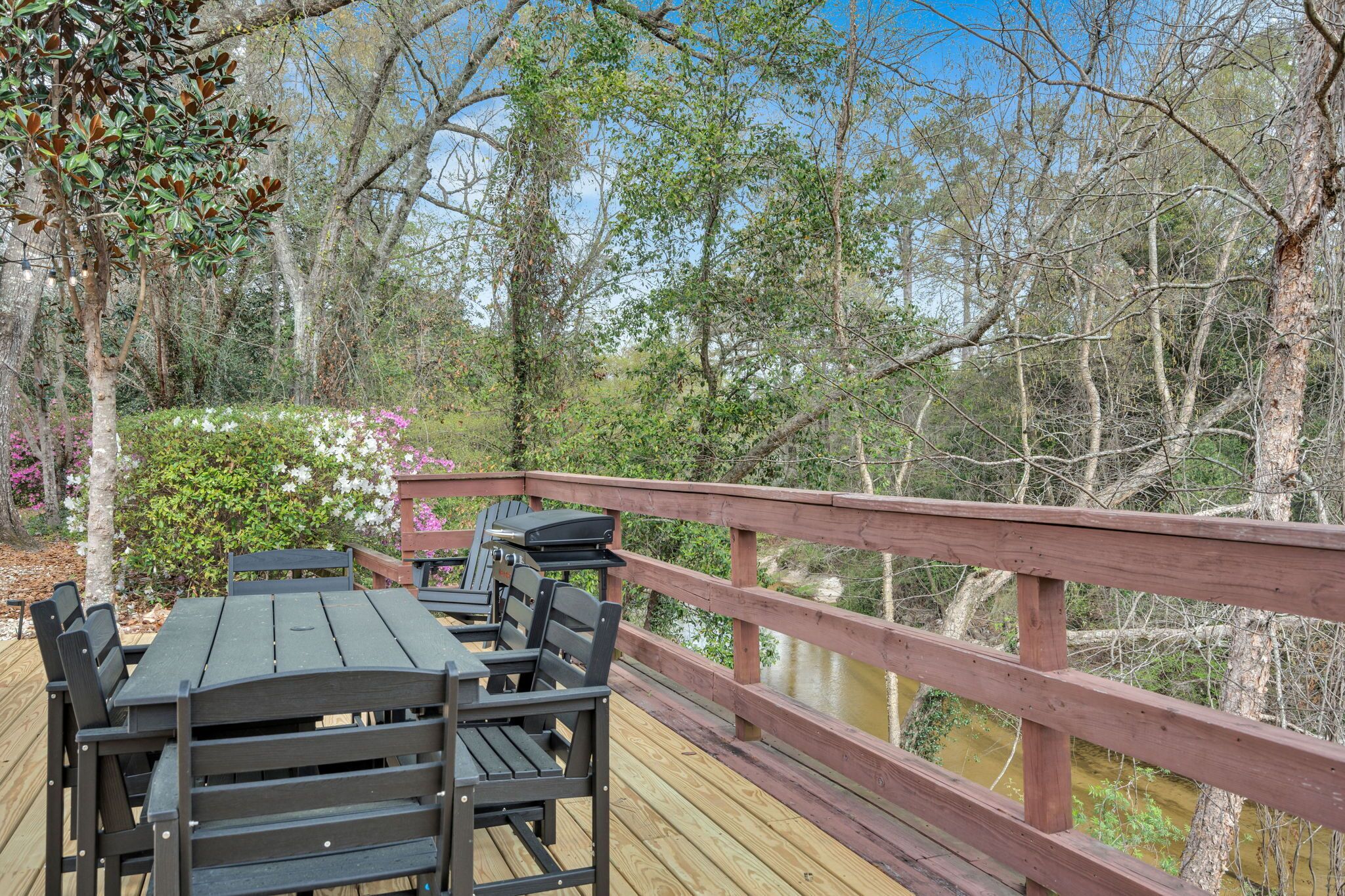 Une terrasse en bois avec une table et des chaises, entourée d’arbres et offrant une vue sur un plan d’eau.