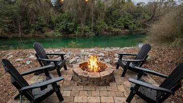 Un foyer entouré de quatre chaises Adirondack, installé sur une terrasse en pierre avec une rivière en arrière-plan.