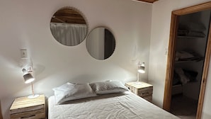Un dormitorio con techo de madera, dos mesitas de noche con lámparas, una cama con ropa blanca y un espejo en la pared.