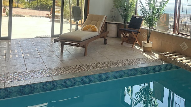 Un área junto a la piscina con una silla de descanso, una mesita y una planta en maceta.