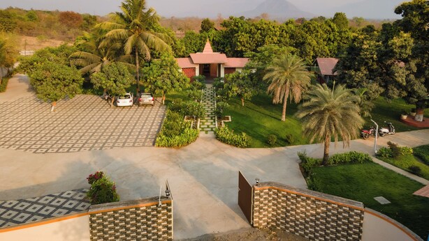 A hotel with a paved courtyard, palm trees, and a mountain in the background. - Glory of MJ, Family Resort in Nature, Panvel (Panvel)