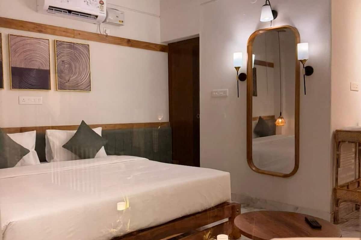 A hotel room with a bed, a wooden headboard, a ceiling fan, an air conditioning unit, a mirror, a small table, and a chair.