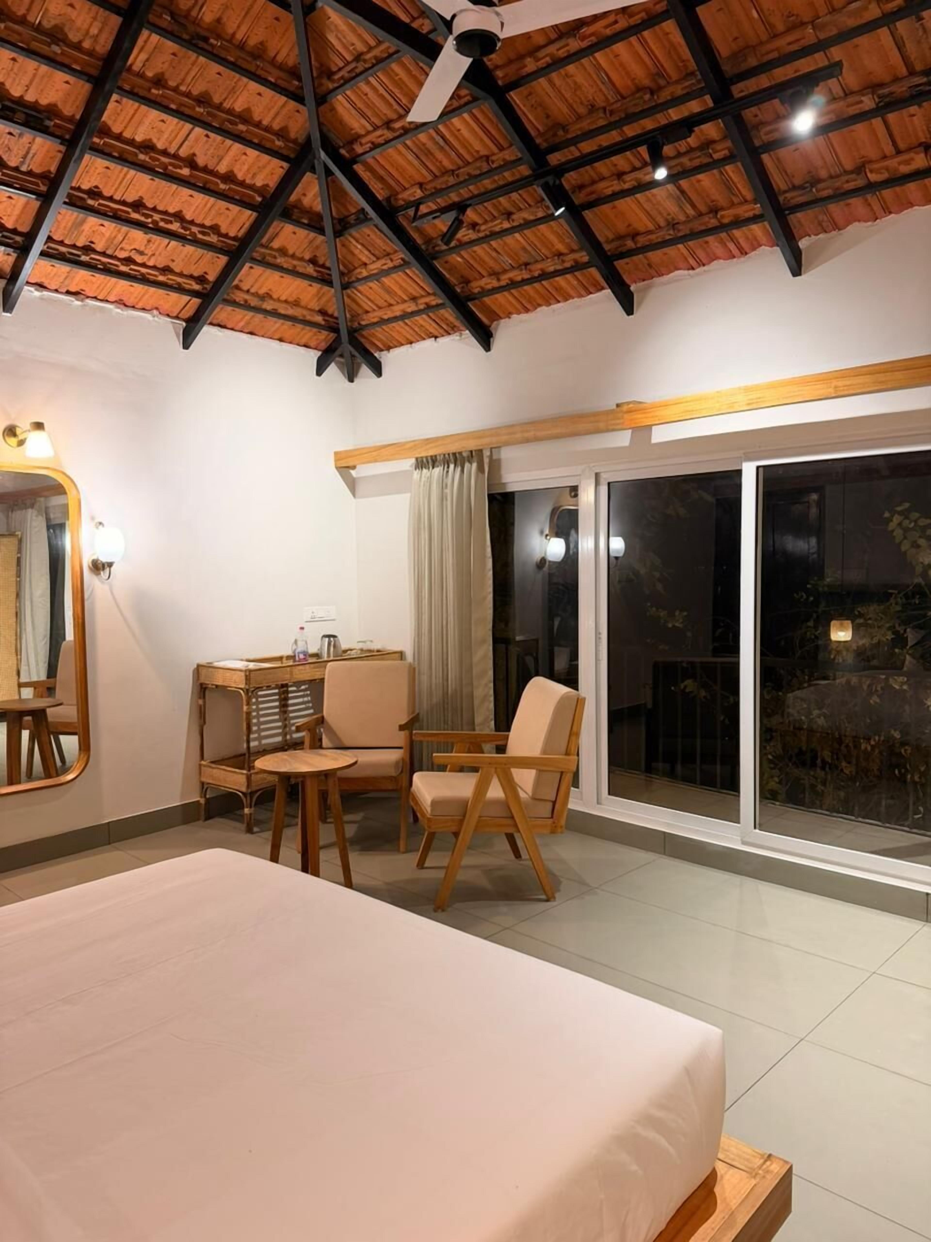 A hotel room with a bed, a desk, a chair, a mirror, and a sliding glass door leading to an outdoor area.
