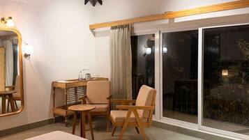 A hotel room with a bed, a desk, a chair, a mirror, and a sliding glass door leading to an outdoor area.