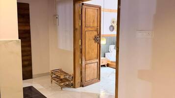 Un couloir avec une porte en bois donnant sur une pièce, un petit banc en osier et un sol en marbre.