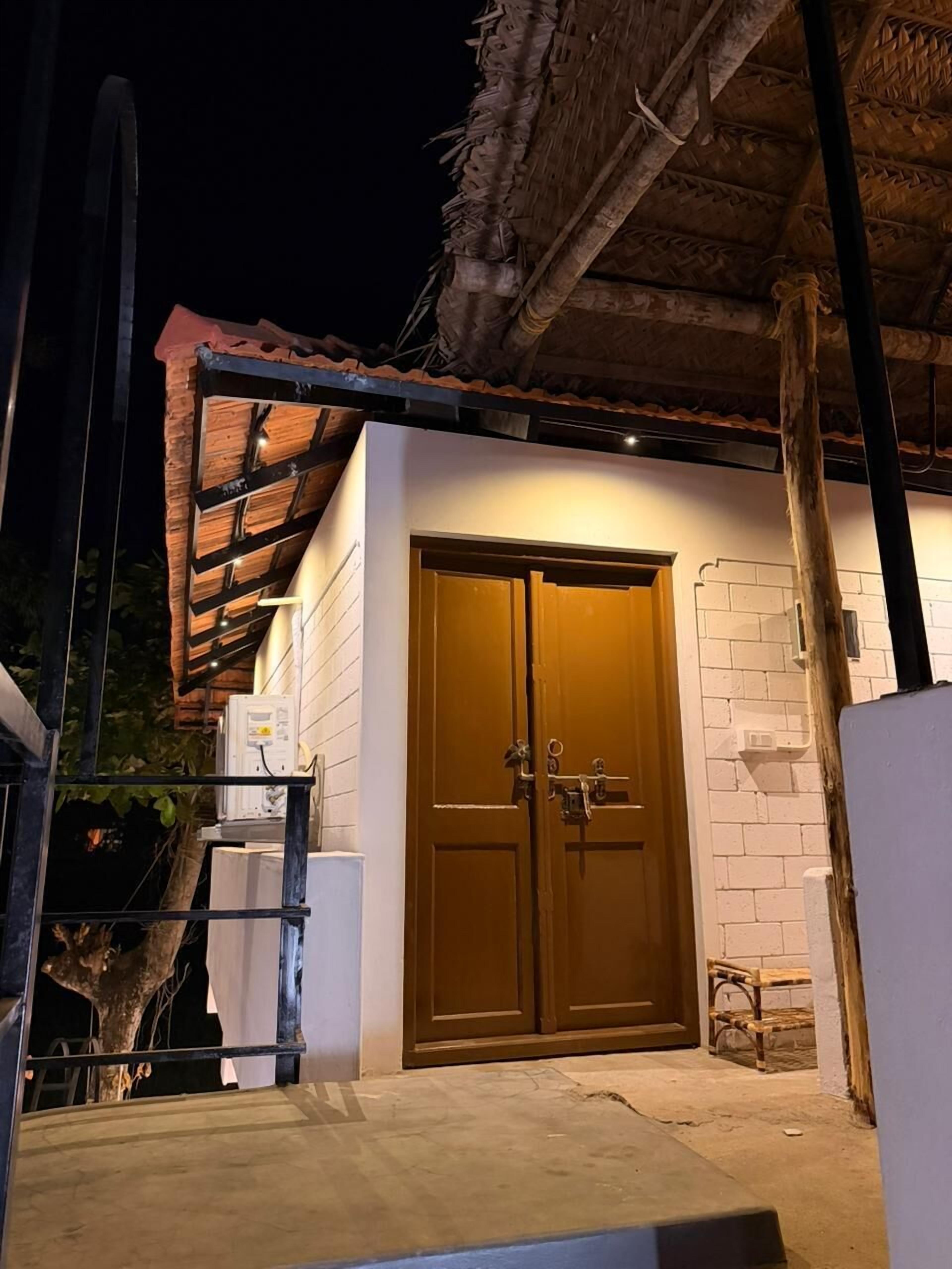 Un edificio con puerta de madera, pared de ladrillo y techo de paja.