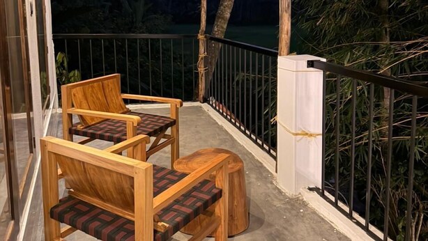 A wooden balcony with two chairs and a table, a thatched roof, and a view of trees. - Bhoomi by Ostello (Varkala)