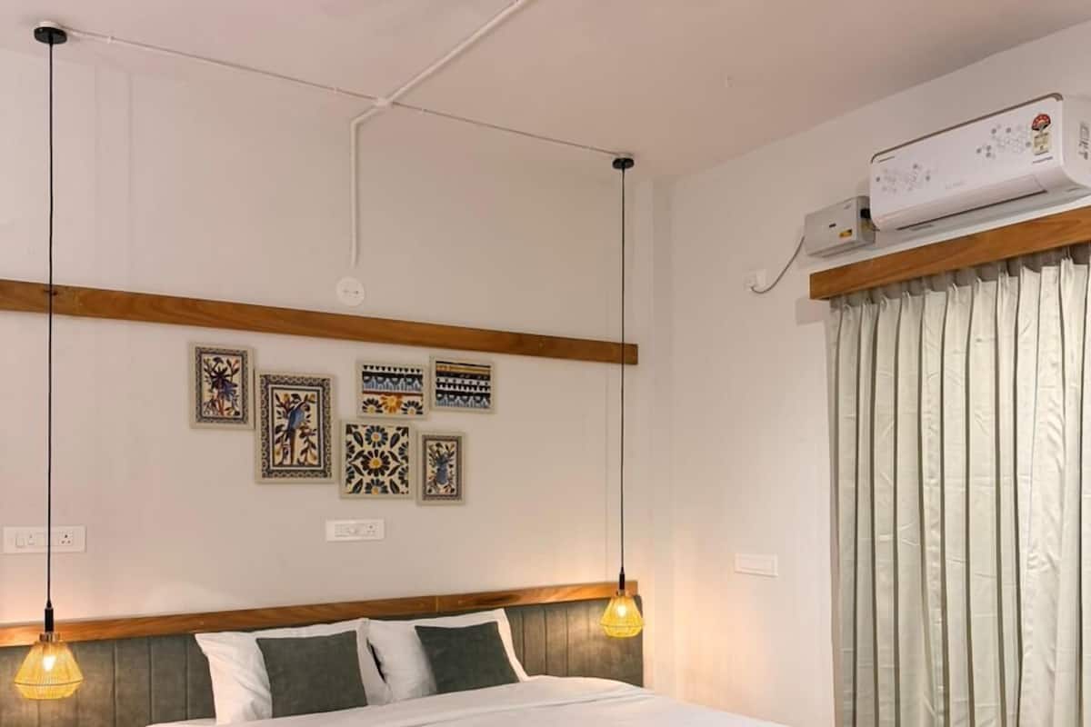 A bedroom with a wooden bed, pendant lights, a ceiling fan, wall art, and an air conditioning unit.