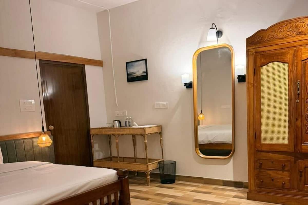 A bedroom with a bed, a round wooden table, a mirror, a wardrobe, and a bedside lamp.
