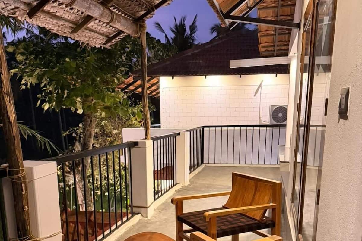 A covered outdoor seating area with wooden furniture and a brick wall in the background.