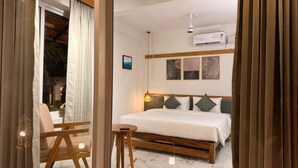 A bedroom with a bed, bedside table, lamp, and artwork on the wall. - Bhoomi by Ostello (Varkala)