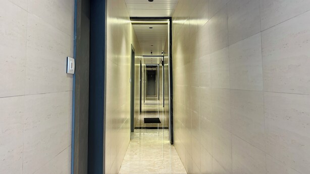 A modern, narrow hallway with a blue accent wall and a glass elevator. - Hotel Imperial Suite (Mumbai)