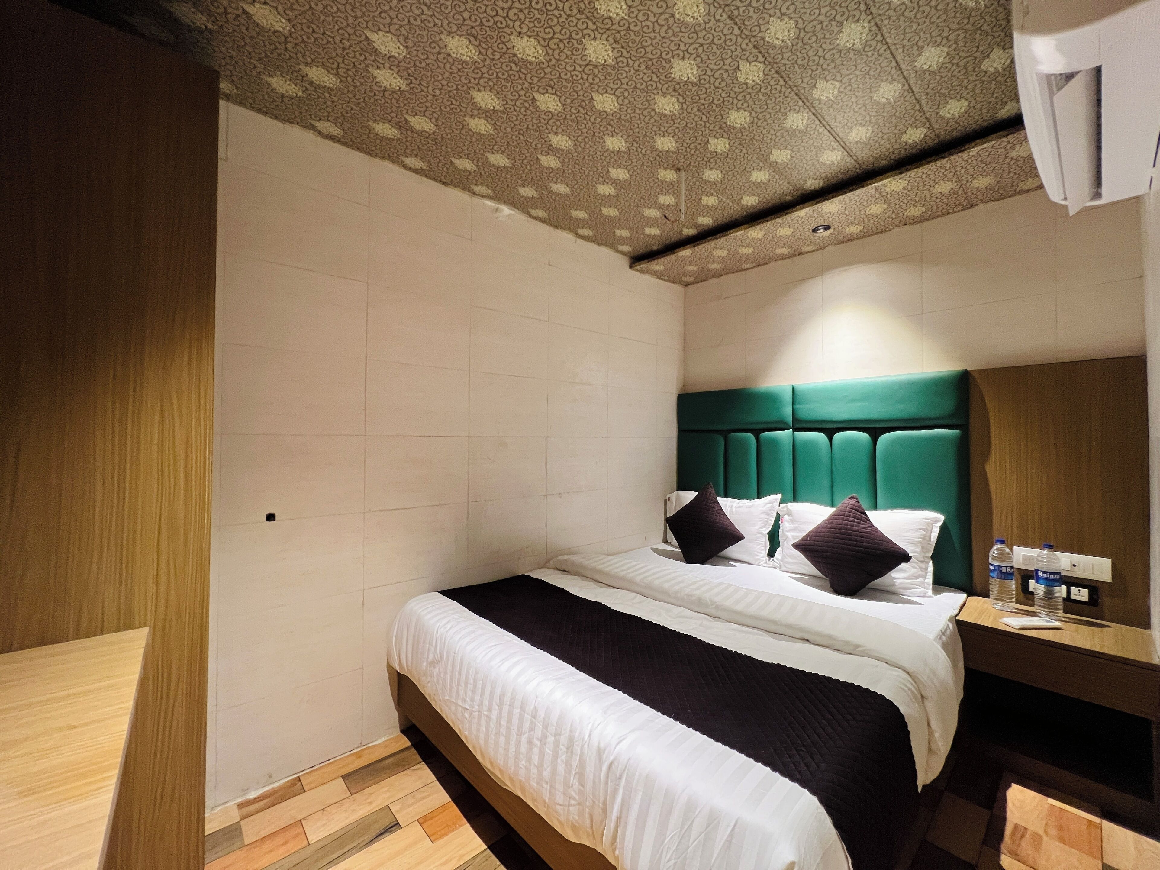 Une chambre d’hôtel avec un lit, un plancher en bois, une tête de lit verte et un plafond à motifs.