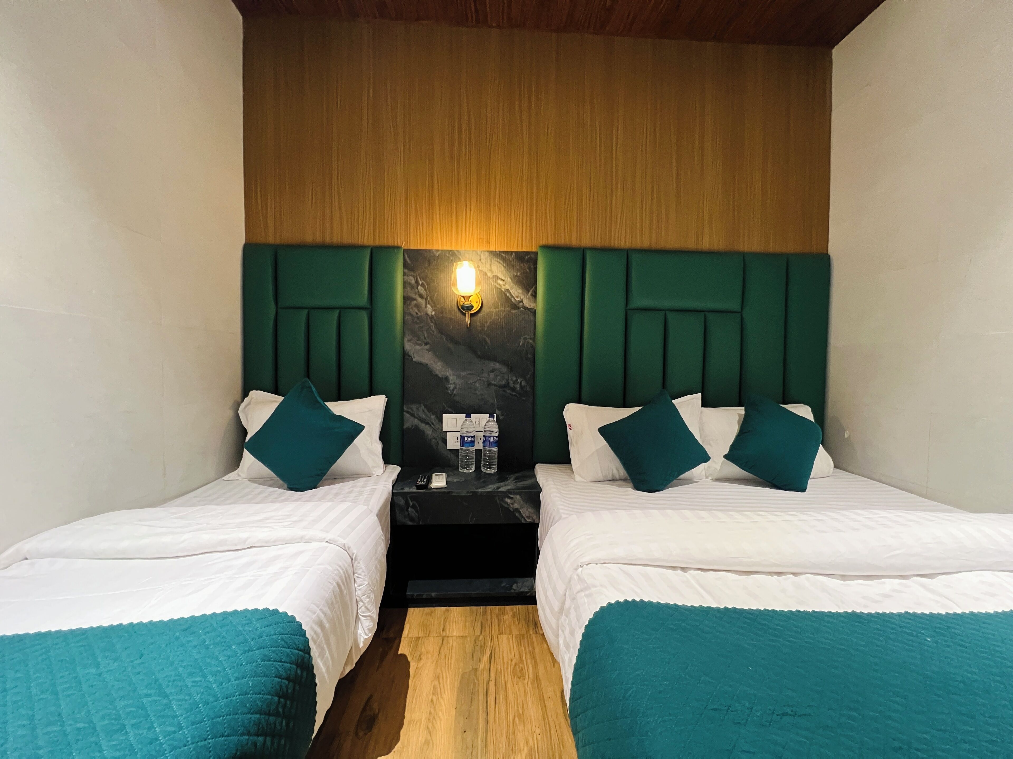 A hotel room with two single beds, a wooden headboard, a marble wall, and a nightstand with a lamp and water bottles.