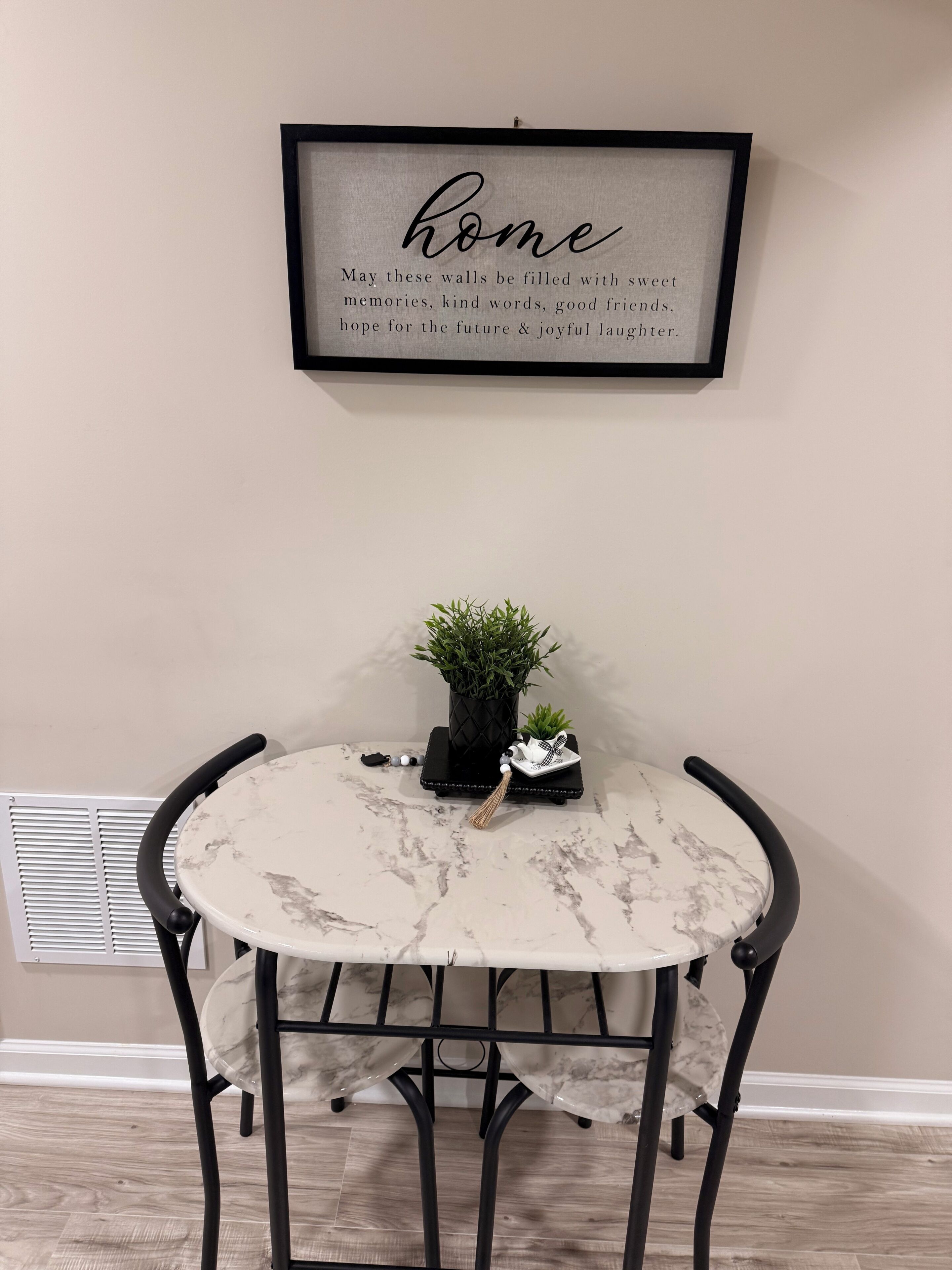 A round table with a marble top, black metal chairs, a framed quote on the wall, a small potted plant, and a decorative item on the table.