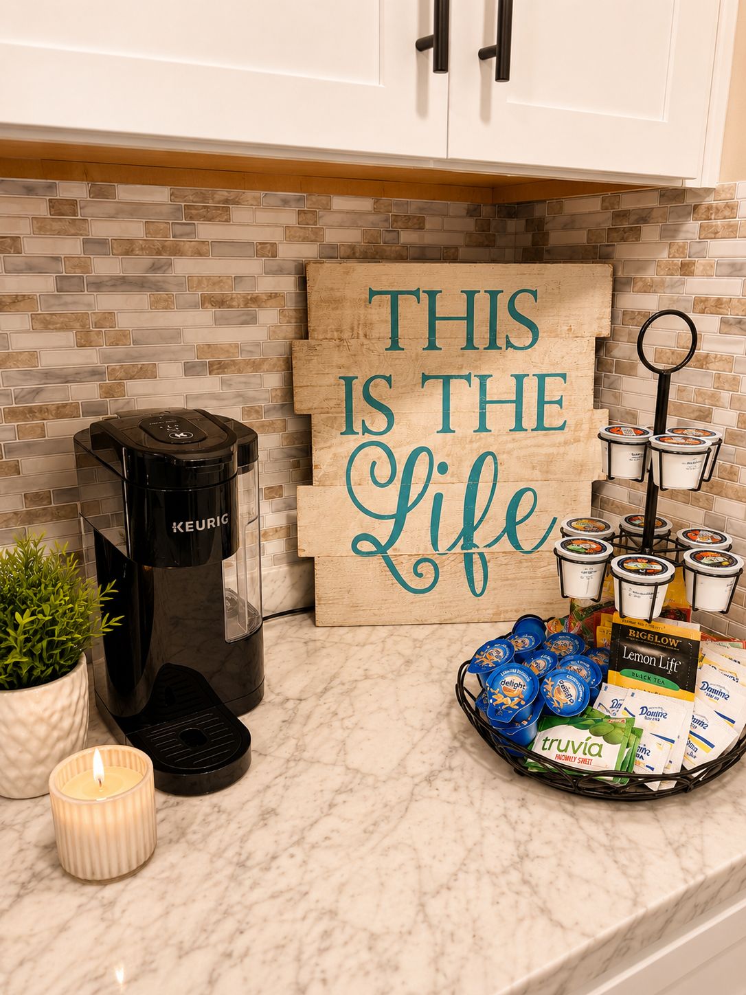 A kitchen with a coffee maker, a sign that says 'THIS IS THE LIFE,' and a tray of food items.