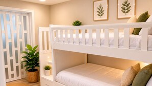 Una cama litera con estructura blanca, una planta pequeña en maceta y una obra de arte con una hoja en la pared.