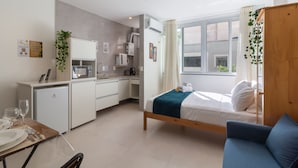 Ein kleines Hotelzimmer mit Bett, einer kleinen Küchenzeile, einem Essbereich und einem Fenster mit Vorhängen.