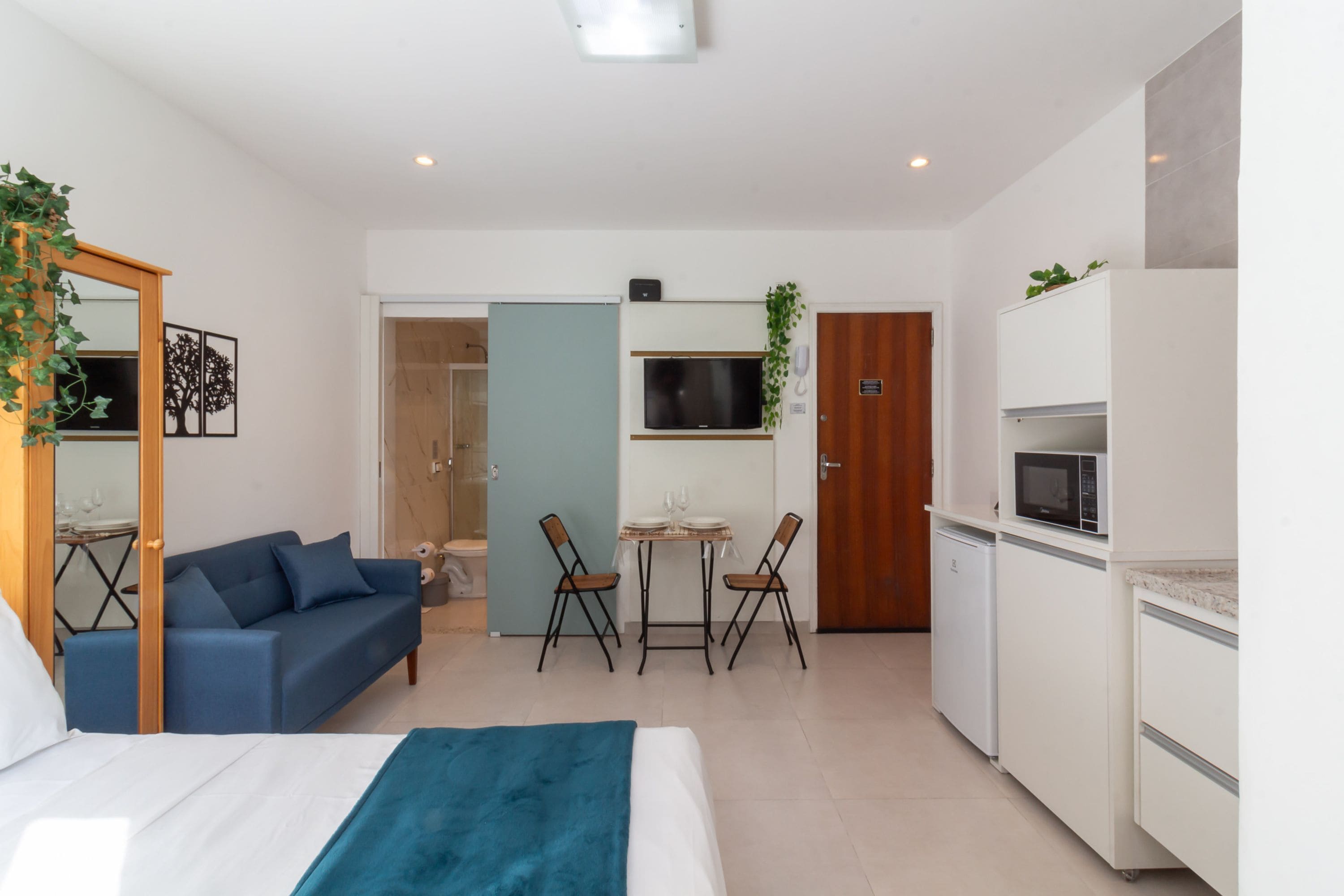 Une chambre d’hôtel moderne équipée d’un lit, d’un canapé bleu, d’une petite table à manger avec des chaises, d’un four à micro-ondes et d’un réfrigérateur.