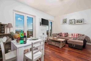 A modern living room with a dining area, large windows, a flat-screen TV, and a sofa with a Union Jack throw blanket. - 2 bedroom Apartment Victoria with panoramic views (Ičići)