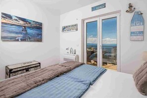 A bedroom with a bed, a painting, a suitcase, and a view of the sea through a sliding door. - 2 bedroom Apartment Victoria with panoramic views (Ičići)