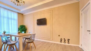 Ein Essbereich mit Holztisch und -stühlen, einem an der Wand befestigten Fernseher und einem Blumentopf.