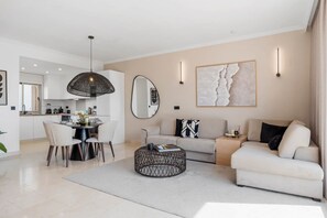 A modern living room with a sofa, a coffee table, and a dining area with chairs and a table. - Luxe 2BR Penthouse | 55m² rooftop – Sea/Pool Views (Estepona)