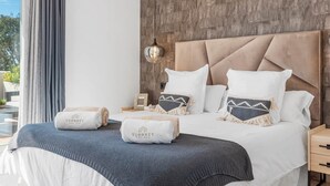 A hotel room with a large bed, a wooden accent wall, a nightstand, and a view of the outdoors. - Luxe 2BR Penthouse | 55m² rooftop – Sea/Pool Views (Estepona)