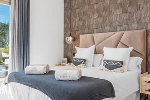 A hotel room with a large bed, a wooden accent wall, a nightstand, and a view of the outdoors. - Luxe 2BR Penthouse | 55m² rooftop – Sea/Pool Views (Estepona)