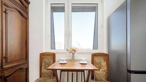 A corner room with a wooden cabinet, a radiator, a table with two chairs, and a refrigerator.