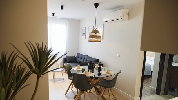 Ein moderner Essbereich mit einem runden Glastisch, grauen Stühlen und einer hängenden Leuchte.